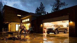 Photo of a husband and wife cleaning up storm debris in their driveway while their Ford F-150 Lightning sits in the garage and provides back-up power to their house.