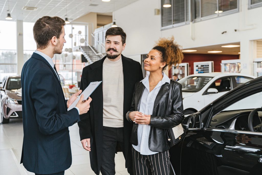 man and woman at car dealership speaking with sales representative