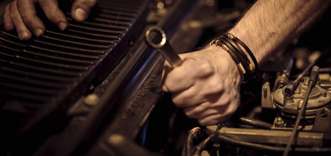 man using wrench to work on truck engine